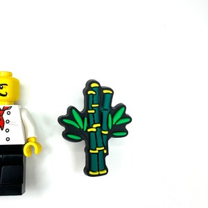 Puede incluir: Un amuleto de planta de bamb&uacute; verde y amarillo con contornos negros. El amuleto est&aacute; hecho de goma y tiene un dise&ntilde;o 3D.