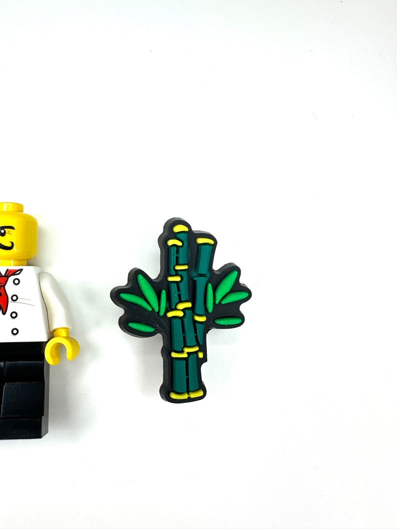 Puede incluir: Un amuleto de planta de bamb&uacute; verde y amarillo con contornos negros. El amuleto est&aacute; hecho de goma y tiene un dise&ntilde;o 3D.