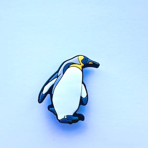 May include: A black and white penguin figurine with a yellow beak and a white belly. The penguin is standing on a light blue background.