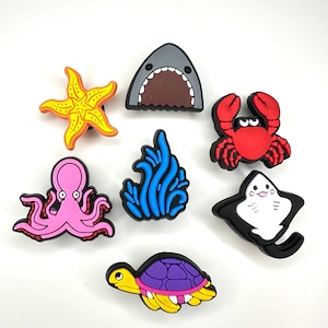 May include: Set of eight colorful sea creature shoe charms. The charms include a shark, starfish, crab, octopus, seaweed, stingray, turtle, and a seahorse.
