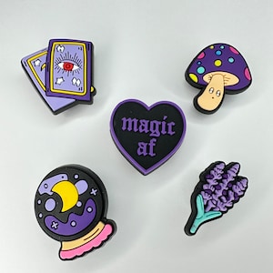 May include: Five purple and black charms with a magical theme. The charms include a tarot card, a heart with the text "magic af", a crystal ball, a mushroom, and a lavender sprig.