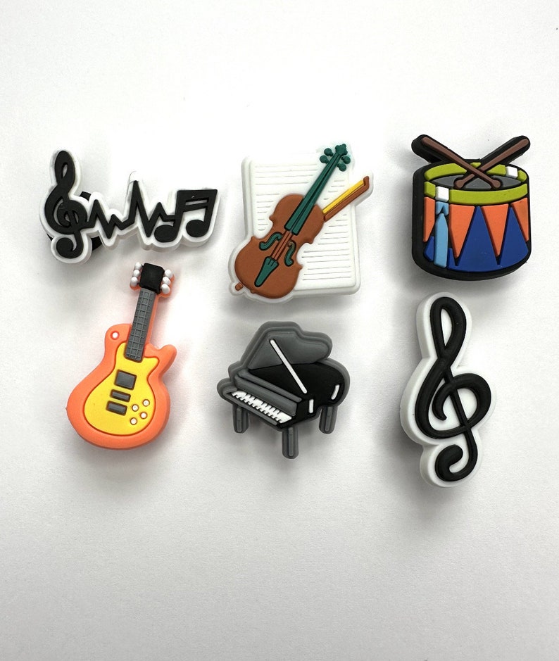 May include: A set of seven colorful musical instrument charms, including a guitar, piano, violin, drum, and treble clef. The charms are made of rubber and are perfect for adding a touch of personality to your belongings.