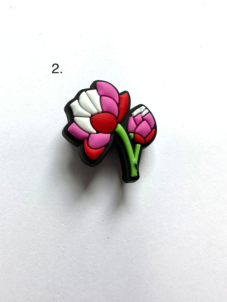 May include: A pink and red flower charm with a green stem and white accents. The charm is made of rubber and has a 3D design.