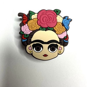 Puede incluir: Una ilustraci&oacute;n de dibujos animados de Frida Kahlo con una corona de flores de colores. La ilustraci&oacute;n est&aacute; en un estilo de dibujos animados con ojos grandes y una boca roja. La corona de flores est&aacute; hecha de flores rosas, amarillas, rojas, azules y verdes.