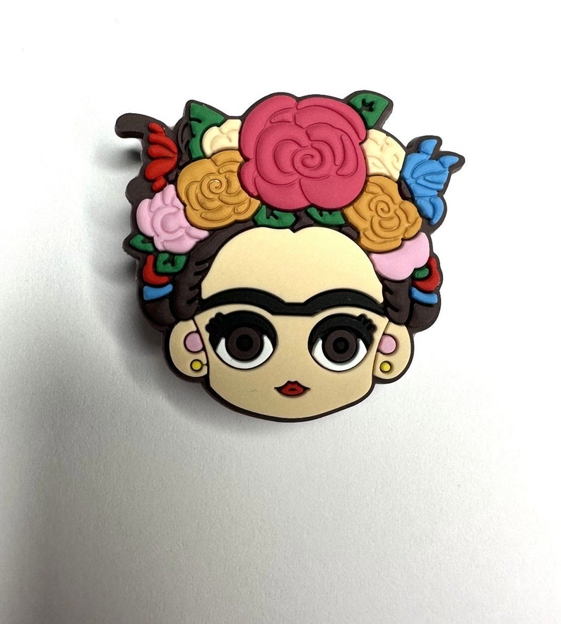 Puede incluir: Una ilustraci&oacute;n de dibujos animados de Frida Kahlo con una corona de flores de colores. La ilustraci&oacute;n est&aacute; en un estilo de dibujos animados con ojos grandes y una boca roja. La corona de flores est&aacute; hecha de flores rosas, amarillas, rojas, azules y verdes.
