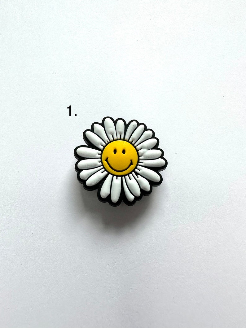 May include: A white daisy with a yellow smiley face in the center. The daisy is black outlined.