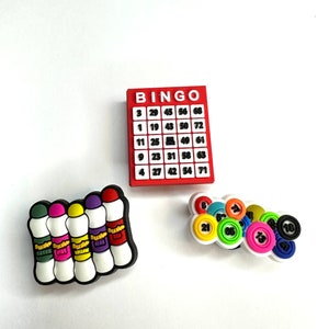 May include: A set of four colourful marker charms and a set of bingo ball charms. The bingo card charm is red with white numbers and the word "BINGO" at the top.