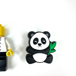 Puede incluir: Una figurita de panda blanco y negro sosteniendo un brote de bamb&uacute; verde. El panda est&aacute; sentado sobre una superficie blanca.