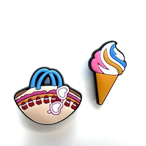 May include: Two decorative charms: a beach bag and an ice cream cone. The beach bag is beige with a blue handle and heart-shaped sunglasses. The ice cream cone has pink, white, blue, and yellow soft serve, with a brown cone.