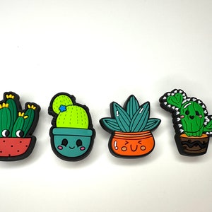Könnte beinhalten: Vier bunte Kaktus- und Sukkulenten-Anhänger mit fröhlichen Gesichtern. Die Anhänger sind aus Gummi und haben ein 3D-Design.