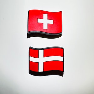May include: Two small, red, fabric flags with white crosses. The flag on the top has a white cross with a thicker center line. The flag on the bottom has a white cross with thinner lines.