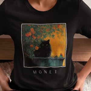 May include: Black t-shirt with a graphic print of a black cat sitting in a garden with flowers. The text "MONET" is printed below the image.