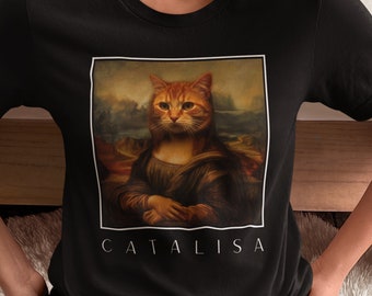 Puede incluir: Camiseta negra con un gráfico de un gato al estilo de la Mona Lisa. El texto "CATALISA" está impreso debajo de la imagen.