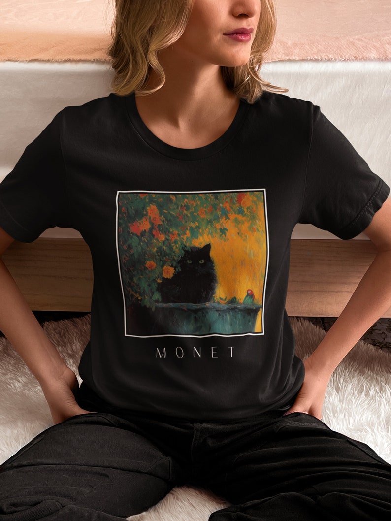 May include: Black t-shirt with a graphic print of a black cat sitting in a garden with flowers. The text "MONET" is printed below the image.