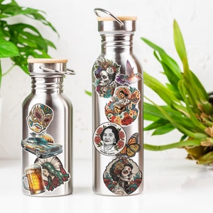 Puede incluir: Dos botellas de agua de acero inoxidable con tapas de bamb&uacute;, adornadas con pegatinas coloridas. Las pegatinas incluyen una m&aacute;scara de luchador, un coche cl&aacute;sico, una jarra de cerveza e im&aacute;genes de Frida Kahlo y dise&ntilde;os florales.