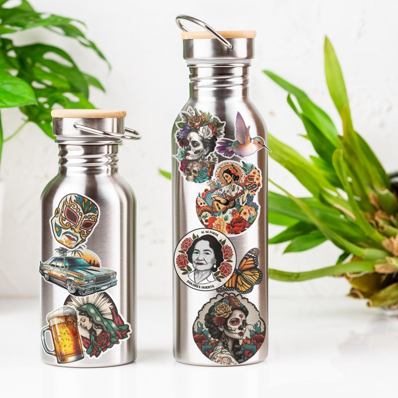 Puede incluir: Dos botellas de agua de acero inoxidable con tapas de bamb&uacute;, adornadas con pegatinas coloridas. Las pegatinas incluyen una m&aacute;scara de luchador, un coche cl&aacute;sico, una jarra de cerveza e im&aacute;genes de Frida Kahlo y dise&ntilde;os florales.
