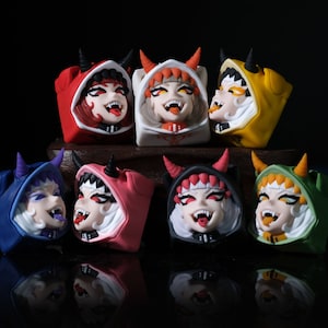 May include: A set of eight colorful keycaps featuring cartoon characters with horns and hooded cloaks. Each keycap has a different color, including red, white, blue, pink, black, green, and yellow.