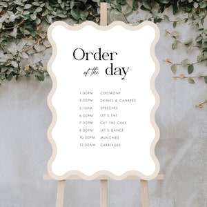 Puede incluir: Un cartel blanco con un borde ondulado y el texto "Order of the day" en negro. El cartel enumera el orden de los eventos de una boda, incluyendo la ceremonia, las bebidas y los canapés, los discursos, la cena, el corte del pastel, el baile y los carruajes.