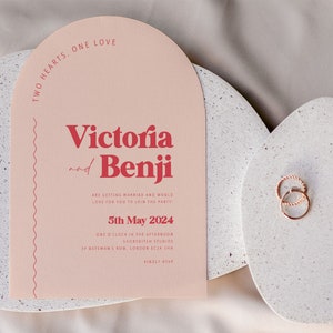 May include: A pink wedding invitation with the text "Two Hearts, One Love" at the top. The names "Victoria and Benji" are in red text. The invitation includes the date "5th May 2024" and the location "Shoreditch Studios, 37 Bateman's Row, London EC2A 3HN".