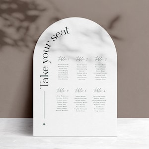 May include: A white, arched wedding seating chart with a marble-like texture. The chart is divided into six tables, each with a list of names. The words "Take your seat" are printed in a dark teal color.
