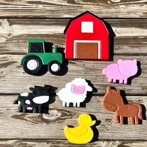 May include: A set of colorful wooden farm animal toys, including a red barn, a green tractor, a white sheep, a black and white cow, a brown horse, a pink pig, and a yellow duck.