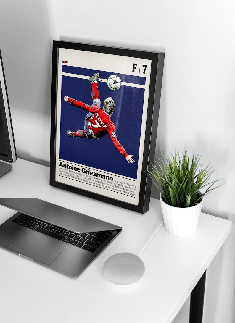 May include: A framed poster featuring a soccer player in mid-air, kicking a soccer ball. The poster is blue and white with the text "F/7 Antoine Griezmann" at the top. The player is wearing a red and white jersey with the number 7 on it.