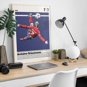 May include: A poster featuring a soccer player in mid-air, kicking a soccer ball. The player is wearing a red jersey with the number 7 on it. The poster has a blue background with the text "F 7" in the top right corner. The text "Antoine Griezmann" is below the image, along with a short biography.