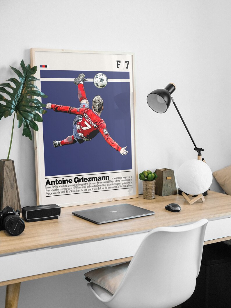 May include: A poster featuring a soccer player in mid-air, kicking a soccer ball. The player is wearing a red jersey with the number 7 on it. The poster has a blue background with the text "F 7" in the top right corner. The text "Antoine Griezmann" is below the image, along with a short biography.