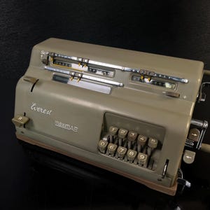 Op de afbeelding: Een olijfgroene Everest MaximAR mechanische rekenmachine. De rekenmachine heeft een numeriek toetsenbord, hendels en wijzerplaten. De namen "Everest" en "maximAR" staan op de voorkant. Vintage kantoormachine.