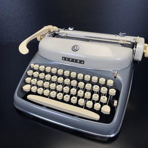 Máquina de escribir Alpina SK24 intacta, año 1961, n.º 273096, QWERTZ, estado impecable, con estuche, manual y certificado.