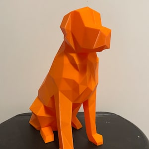 May include: Orange geometric dog sculpture made of plastic. The dog is sitting with its head turned to the side.