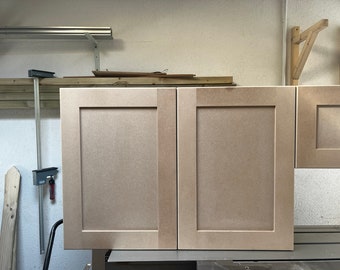 May include: Two unfinished wood cabinet doors with a raised panel design. The doors are light brown and have a smooth surface.