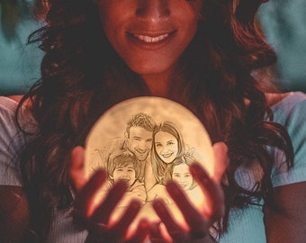 May include: A person holding a glowing moon-shaped lamp with a family photo etched into the surface. The photo shows a couple and two children.