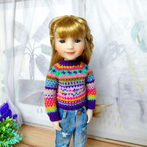 Può includere: Una bambola con i capelli biondi indossa un maglione lavorato a maglia colorato e jeans blu. Il maglione presenta un vivace motivo a righe rosa, verdi, blu e gialle. I jeans della bambola hanno dettagli strappati.