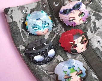 May include: Five circular pins featuring stylized anime-inspired character faces attached to a grey and white camouflage-patterned fabric bag. The pins display various designs including a masked figure, a character with sunglasses, a red-haired figure, a black spider-web patterned mask, and a character with green accents.