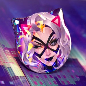 May include: A cat-shaped pin with a winking woman's face, featuring white hair, a black mask, and dark lipstick. The pin has a holographic, iridescent finish with pink and yellow accents. The background is a purple cityscape.