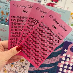 May include: Three pink cards with a savings challenge theme. The cards are labelled "50p Savings Challenge", "£1 Savings", and "£2 Savings Challenge". Each card has a grid of circles with the amount to save written inside each circle. The cards are designed to help people save money.
