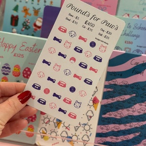 May include: A white card with the title "Pound's for Paw's Challenge" and a budget for pet supplies. The card has a variety of stickers on it, including bones, dog bowls, cats, and balls. The stickers are in pink, blue, and purple.