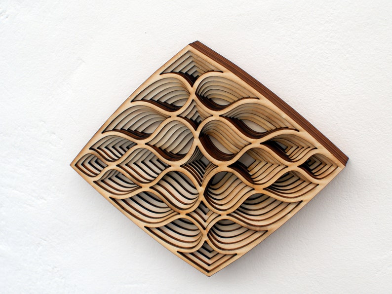 May include: A wooden wall art piece with a geometric design of overlapping, layered curves. The piece is made of light brown wood and has a diamond shape.