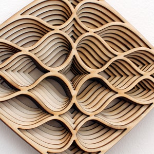 May include: A wooden wall art piece with a geometric design of overlapping, layered, and curved shapes. The piece is made of light brown wood and has a diamond shape.