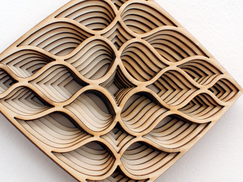 May include: A wooden wall art piece with a geometric design of overlapping, layered, and curved shapes. The piece is made of light brown wood and has a diamond shape.
