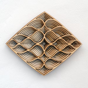 May include: A wooden wall art piece with a geometric design of overlapping, layered shapes. The design is reminiscent of a wave or water pattern. The piece is made of light brown wood and has a natural finish.