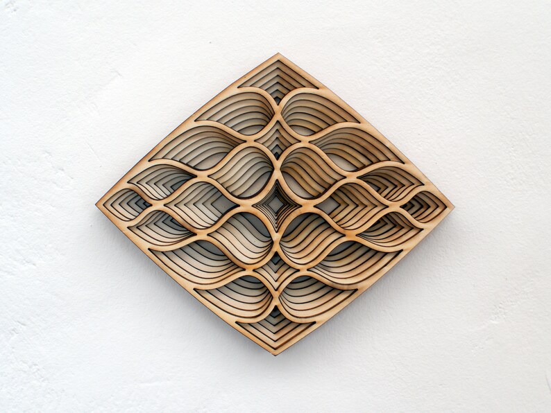 May include: A wooden wall art piece with a geometric design of overlapping, layered shapes. The design is reminiscent of a wave or water pattern. The piece is made of light brown wood and has a natural finish.