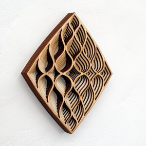 May include: A wooden wall art piece with a geometric design. The design is made up of overlapping layers of wood, creating a 3D effect. The wood is a light brown color with darker brown accents.