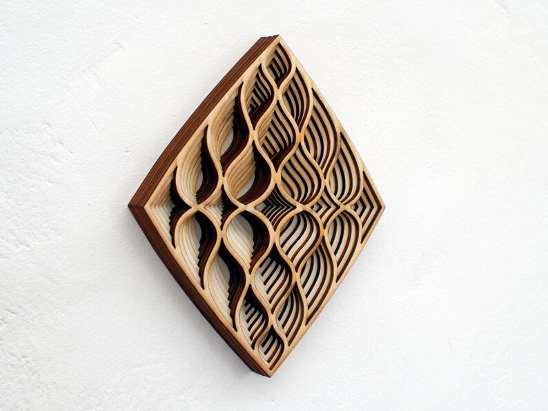 May include: A wooden wall art piece with a geometric design. The design is made up of overlapping layers of wood, creating a 3D effect. The wood is a light brown color with darker brown accents.