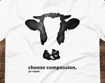 Op de afbeelding: Wit T-shirt met een zwart-wit silhouet van een koeienkop en de tekst "choose compassion. go vegan."