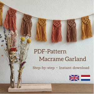 Op de afbeelding: Een PDF-patroon voor een macramé-slinger met een stapsgewijze handleiding. De slinger is gemaakt van bruin, oranje en geel garen en hangt aan een witte muur. De tekst "PDF-Pattern Macrame Garland Step-by-step ~ Instant download" is zichtbaar onder de slinger. De afbeelding toont ook twee glazen vazen met gedroogde bloemen op een houten oppervlak. De vlaggen van het Verenigd Koninkrijk en Nederland zijn zichtbaar in de rechterbenedenhoek.