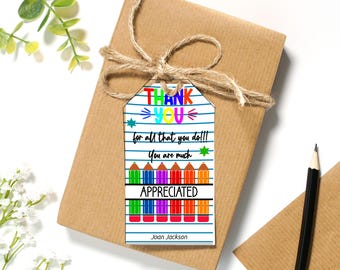 May include: A rectangular paper gift tag with a white background featuring blue horizontal lines, colorful pencil illustrations, and the text THANK YOU for all that you do!!! You are much APPRECIATED and the name Joan Jackson printed at the bottom.