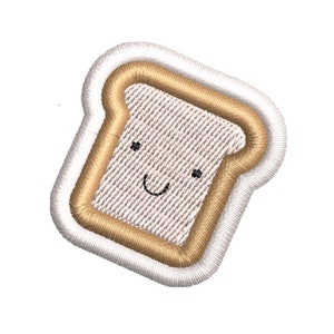 K&ouml;nnte beinhalten: Ein wei&szlig;er und brauner gestickter Aufn&auml;her in Form einer Scheibe Brot mit einem l&auml;chelnden Gesicht.