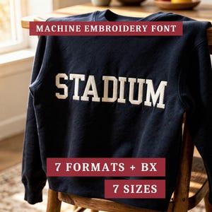 May include: A dark navy blue long-sleeve sweatshirt featuring the word STADIUM embroidered in white block letters across the chest. Text overlays on the image read MACHINE EMBROIDERY FONT, 7 FORMATS + BX, and 7 SIZES in white on red banners.